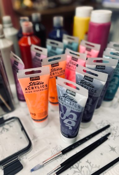 Assorted art paint tubes in various colours, alongside brushes and a palette.