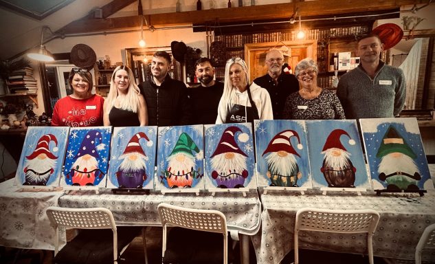 A group of people stands behind painted gnome artworks on display.