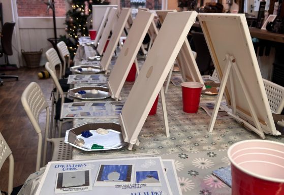 Row of easels set up for a painting activity, with trays and coloured paint nearby.
