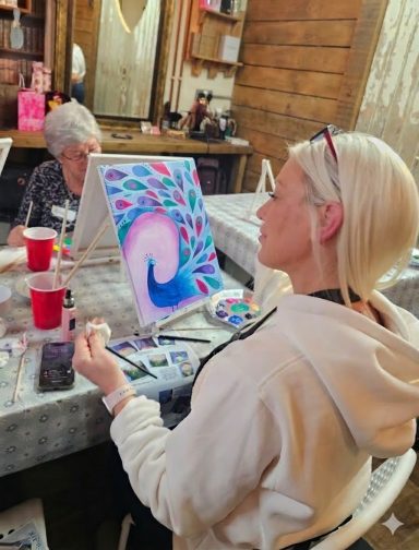 A woman painting on a canvas while another person creates art in a relaxed setting.