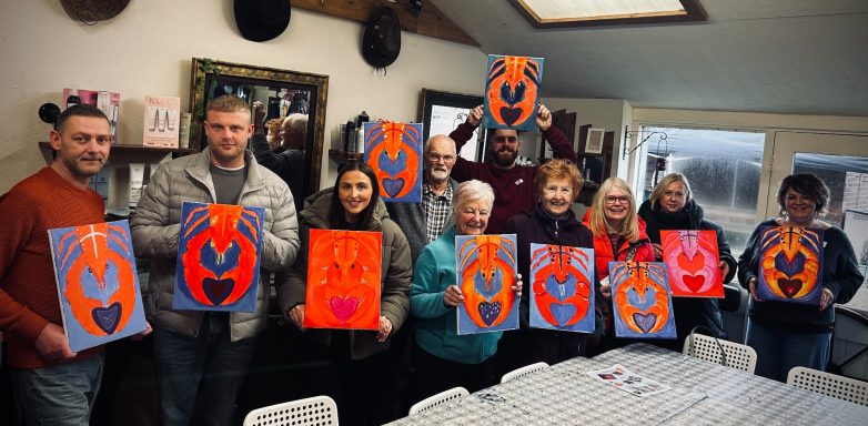 Group of people holding painted canvases with orange and blue designs in a studio setting.